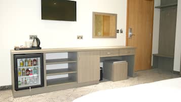 Una habitación de hotel con minibar, televisión, espejo y puerta de madera.