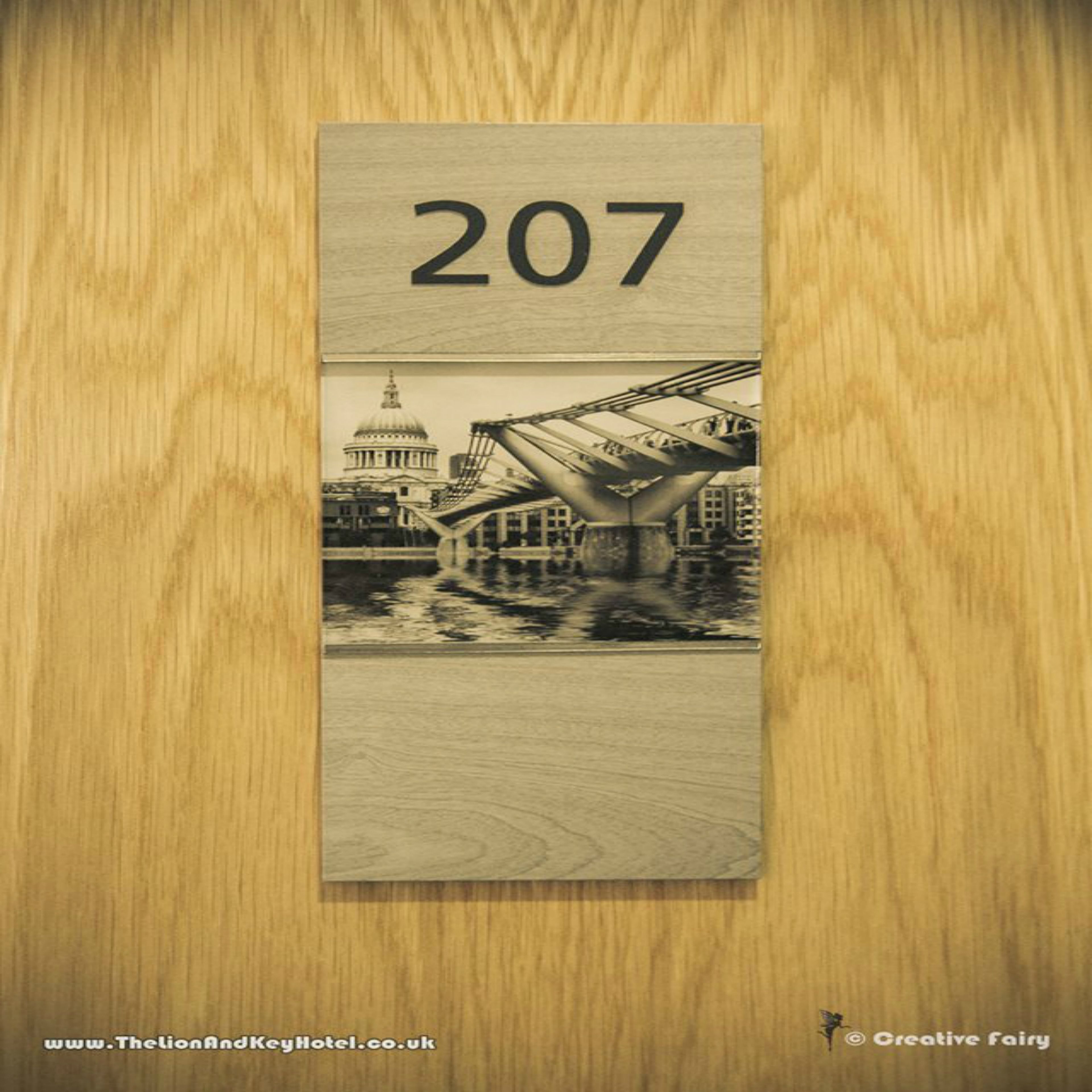 Puerta de madera con el número '207' y una fotografía blanco y negro de un puente sobre un río, con edificios al fondo.