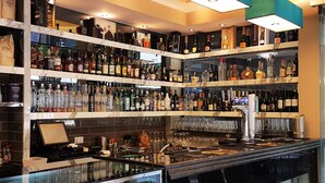 Zona de bar amb diverses prestatgeries plenes de diferents ampolles de licors, una caixa registradora i una vitrina de vidre.