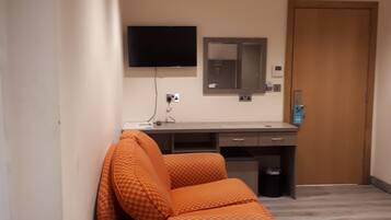 A hotel room with a sofa, a desk, a flat-screen TV, a mirror, and a door.