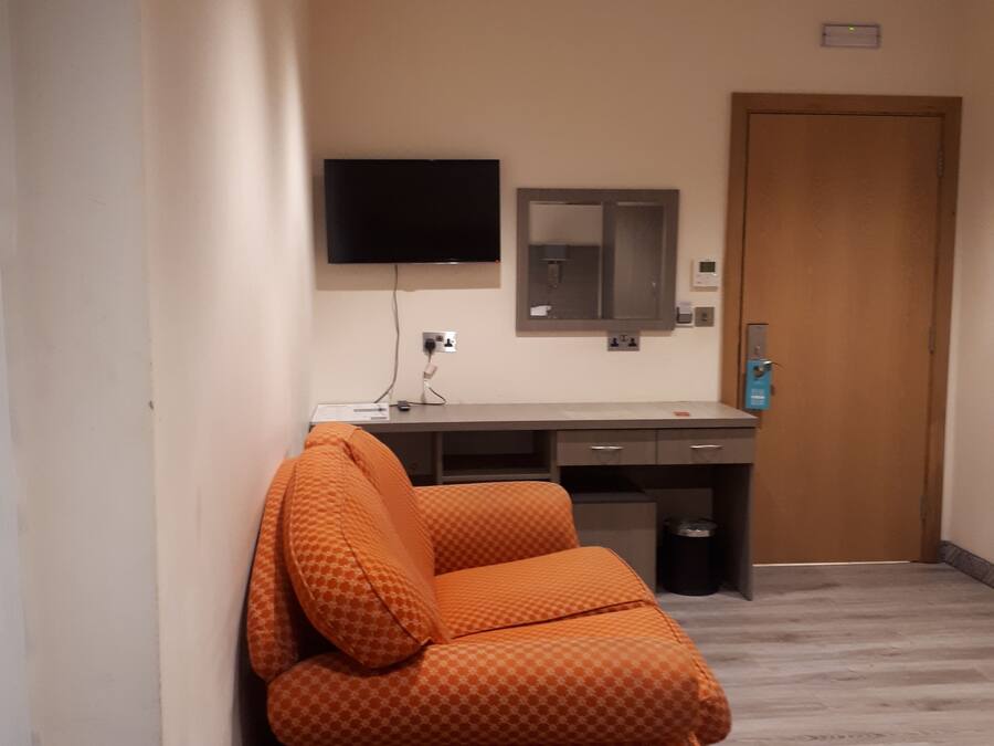 A hotel room with a sofa, a desk, a flat-screen TV, a mirror, and a door.