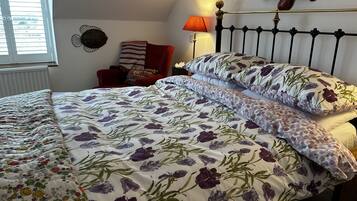 A neatly made bed with floral bedding, a bedside table with a lamp, and a chair with a patterned cushion.