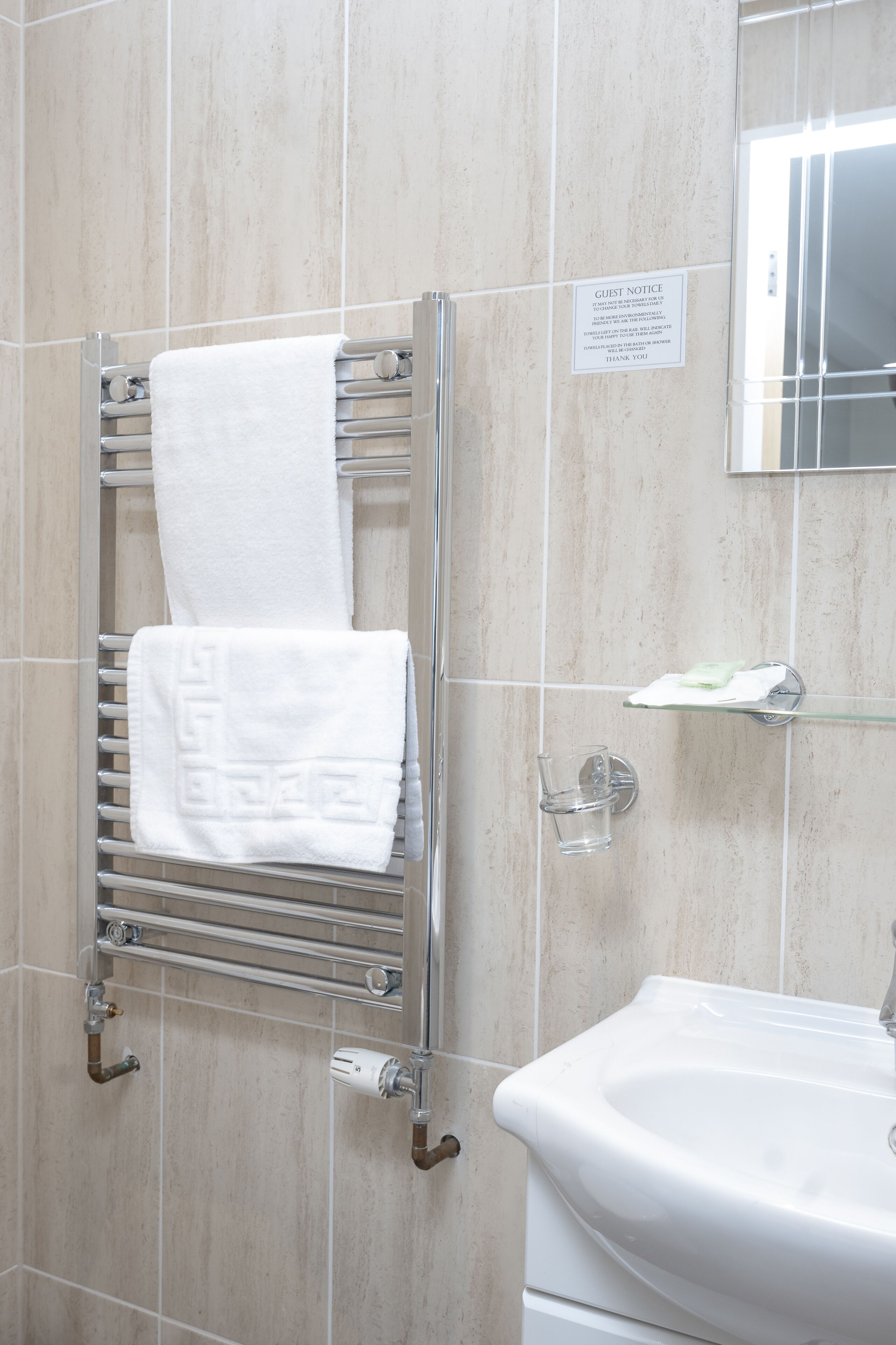 A bathroom with a towel rack holding two white towels, a glass shower enclosure, and a sink with a mirror above it.