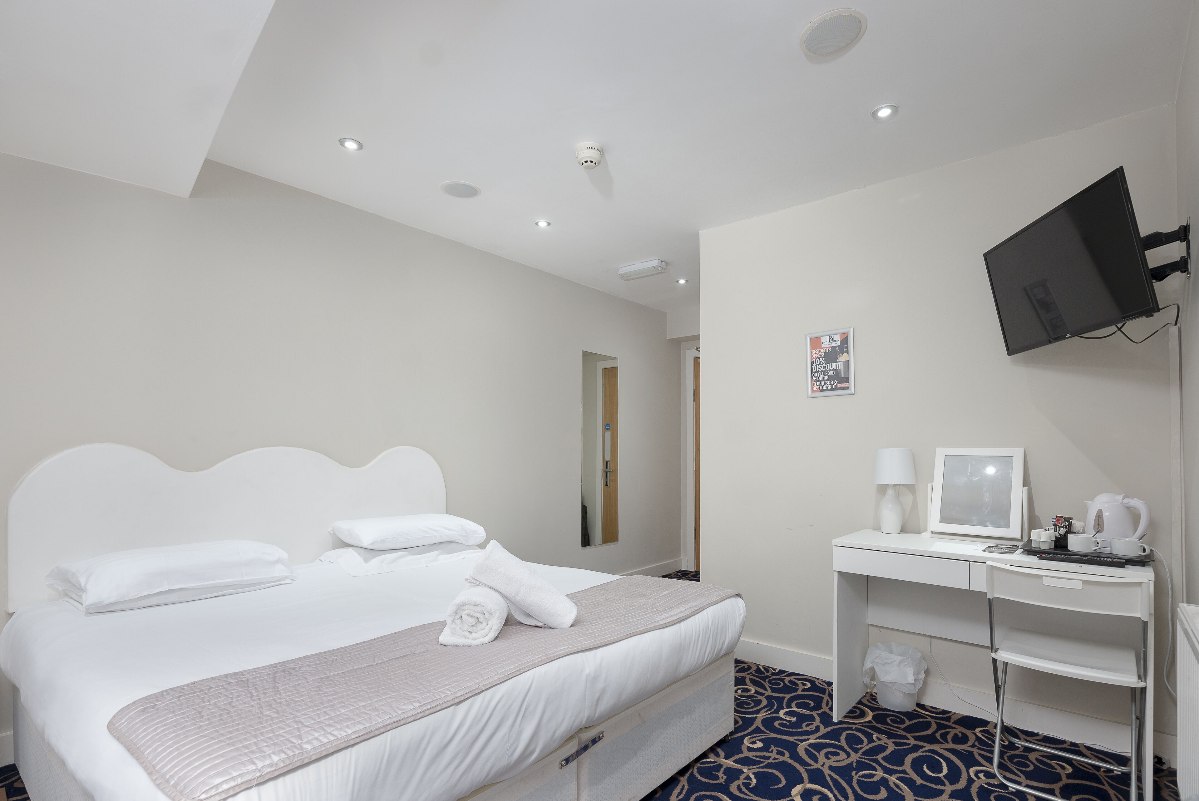 Une chambre d’hôtel équipée d’un lit, d’un bureau avec un ordinateur, d’une télévision et d’une machine à café.