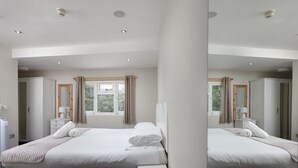 A hotel room with a large bed, a bedside table, a mirror, and a window with curtains.