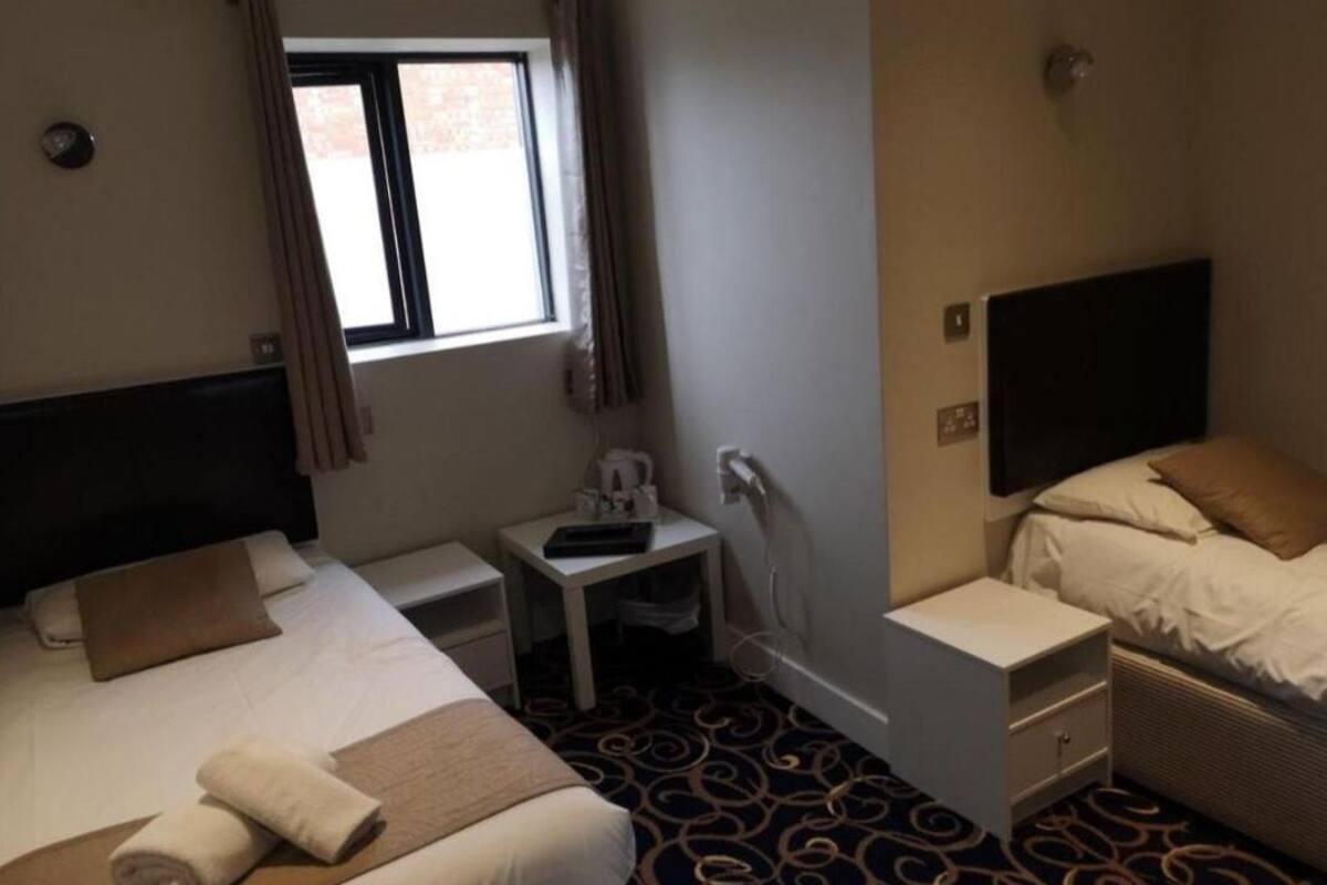 A hotel room with two beds, a small desk, a flat-screen TV, and a window with curtains.