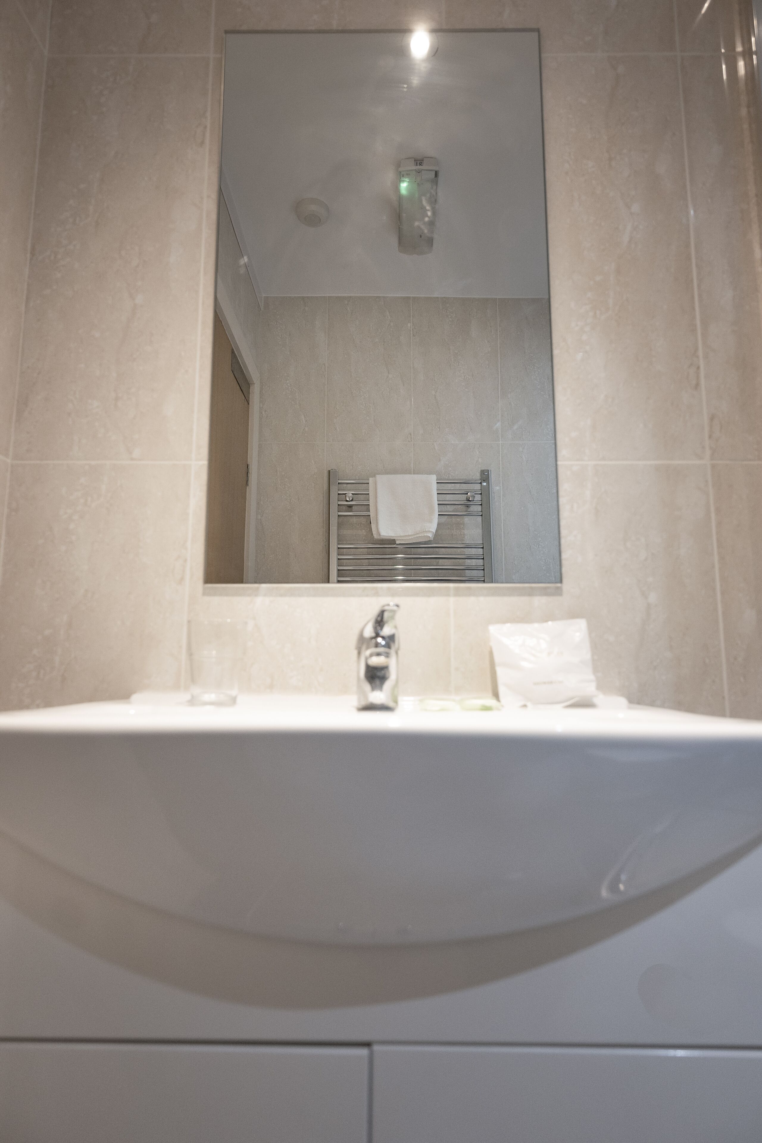 Un baño con un espejo grande, un lavabo y un perchero para toallas.