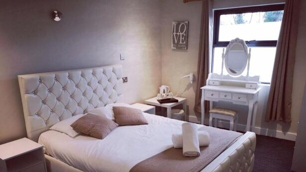 A neatly arranged hotel room with a large bed, a bedside table, a vanity with a mirror, and a window with curtains.