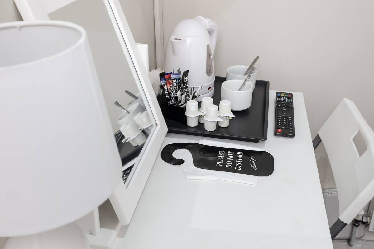A white desk with a coffee maker, a tray with cups and a spoon, a remote control, and a "Please do not disturb" sign.