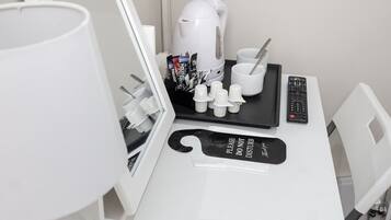 Un escritorio blanco con una cafetera, una bandeja con tazas y una cuchara, un control remoto y un cartel que dice 'No molestar'.