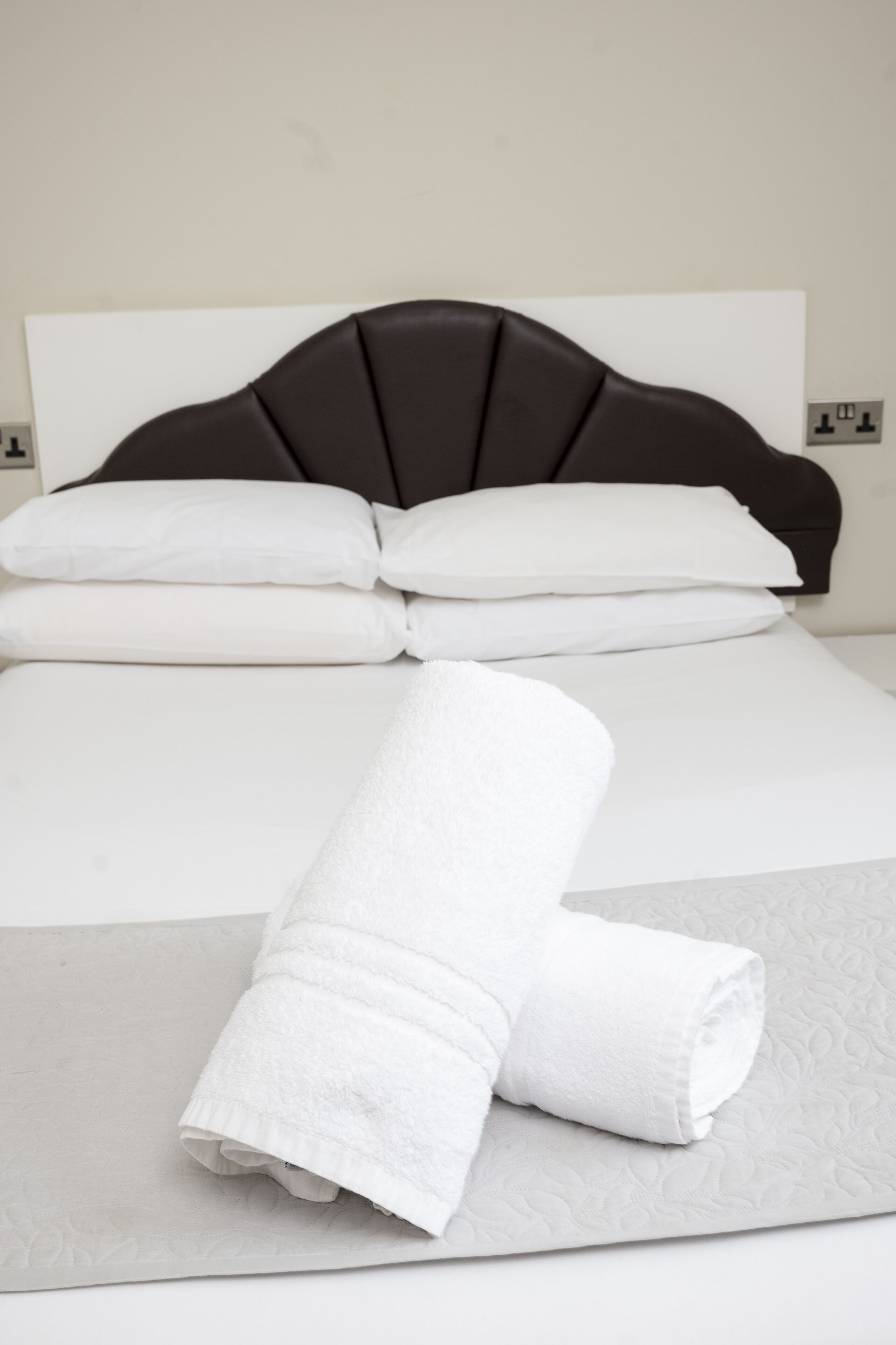 A neatly made bed with white linens and a folded towel on a grey bedspread.