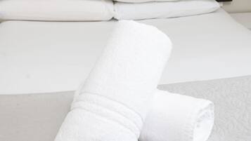 A neatly made bed with white linens and a folded towel on a grey bedspread.