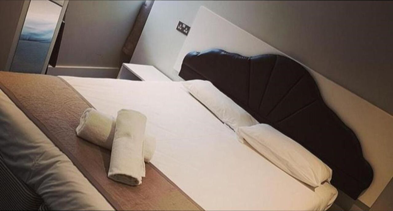A hotel room with a bed, a wooden side table, and a window.