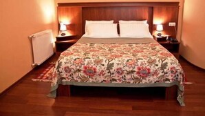A neatly made bed with a floral bedspread, two bedside tables with lamps, and a radiator on the wall. - Astoria Hotel Tbilisi (Tbilisi)