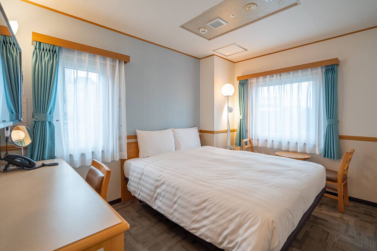 Une chambre d’hôtel avec un grand lit, un bureau avec un téléphone, deux chaises et une lampe.