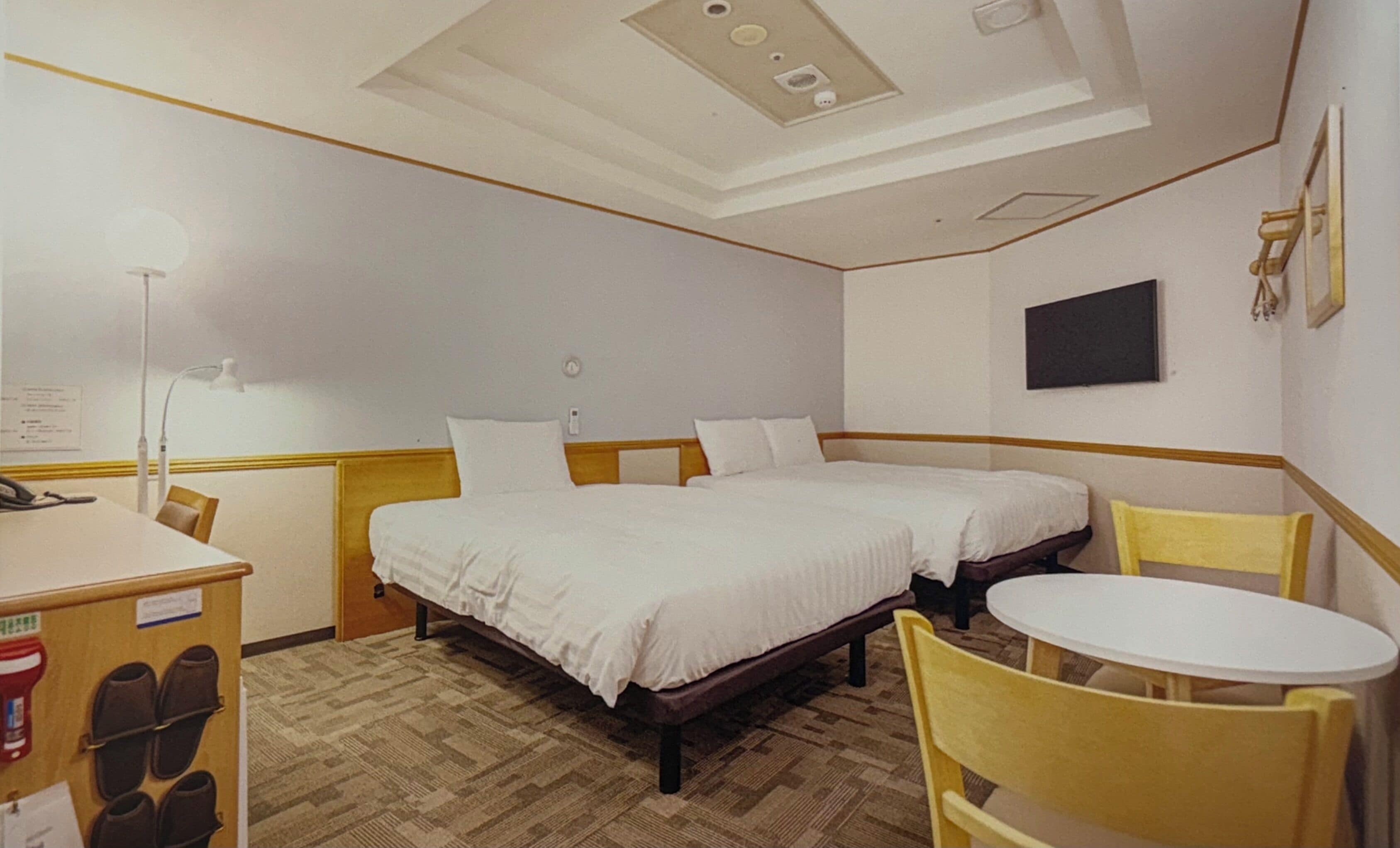 Een hotelkamer met twee bedden, een bureau, een stoel, een tafeltje en een aan de muur bevestigde televisie.