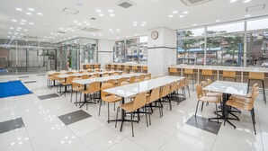 A spacious cafeteria with multiple dining tables and chairs, large windows offering a view of the city, and a clock on the wall. - Toyoko Inn Seoul Dongdaemun 1 (Seoul)