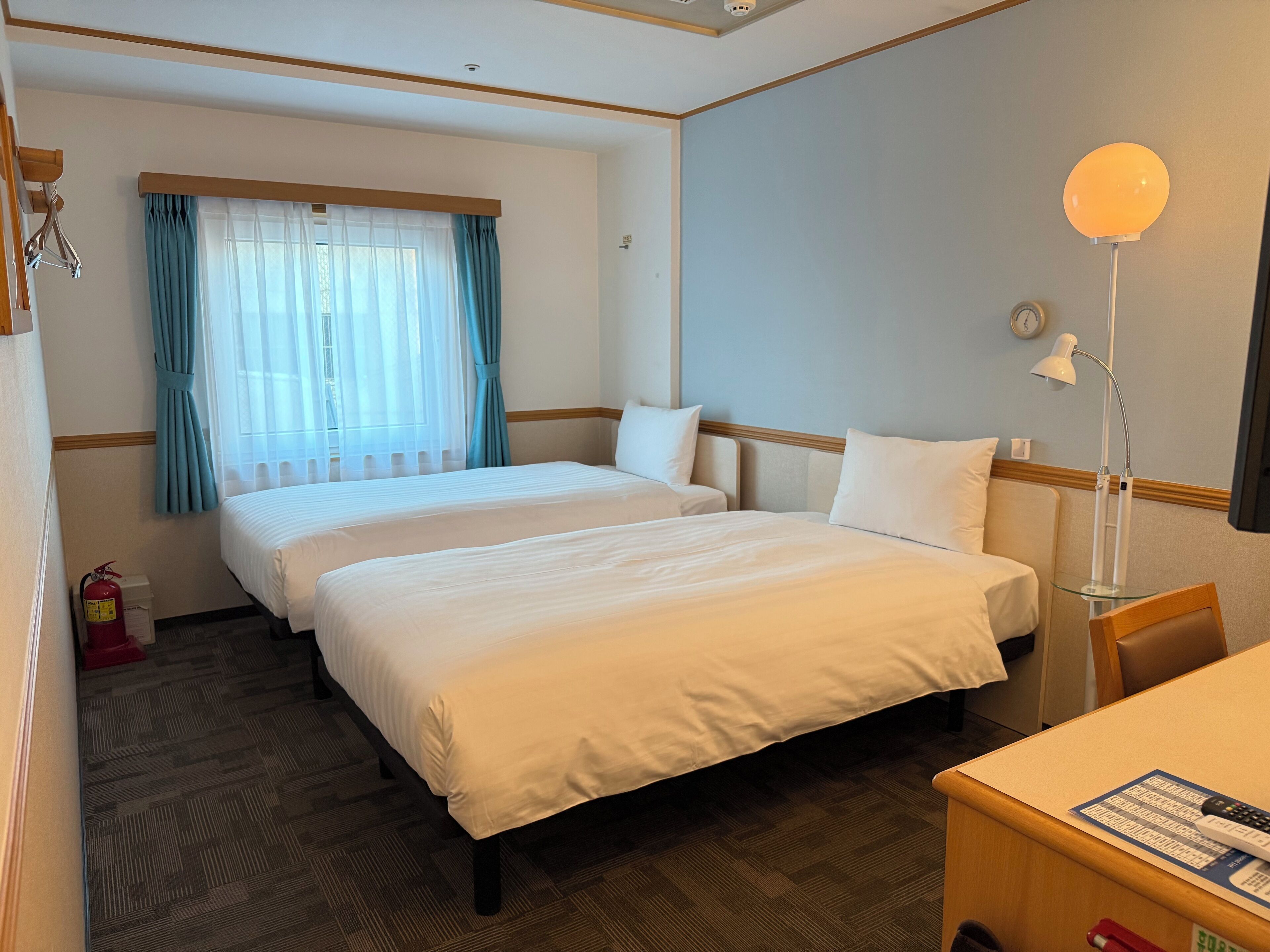 Una habitación de hotel con dos camas, un escritorio, una lámpara y un extintor.