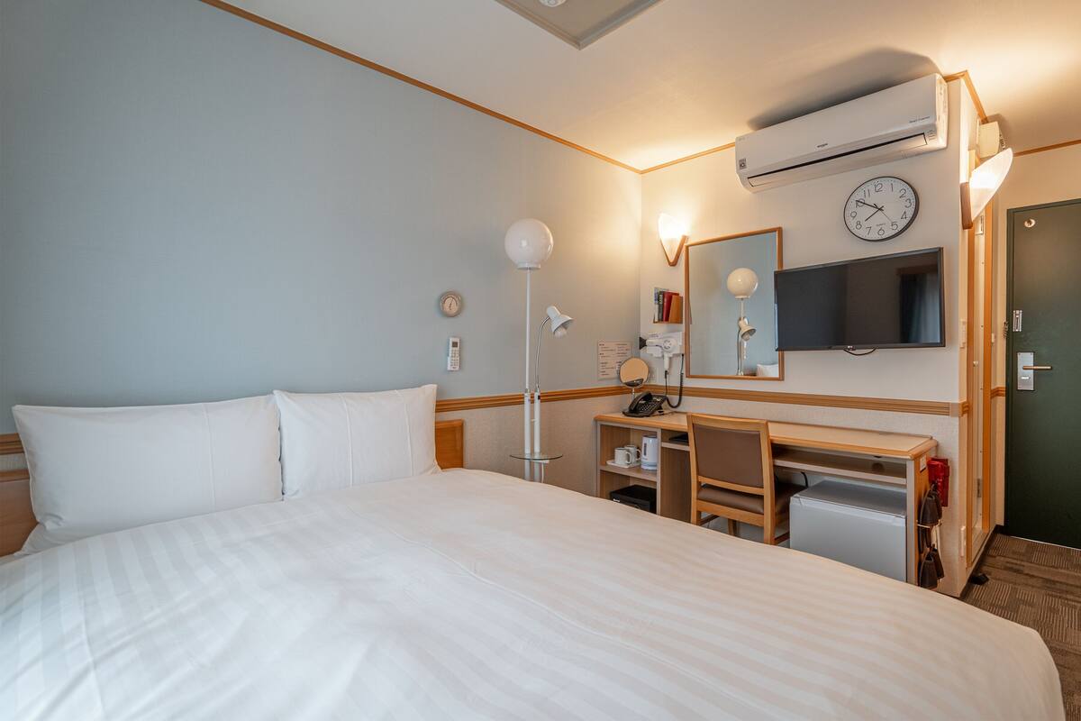 Une chambre d’hôtel dotée d’un grand lit, d’un bureau avec une chaise, d’un téléviseur à écran plat, d’un miroir et d’un appareil de climatisation.