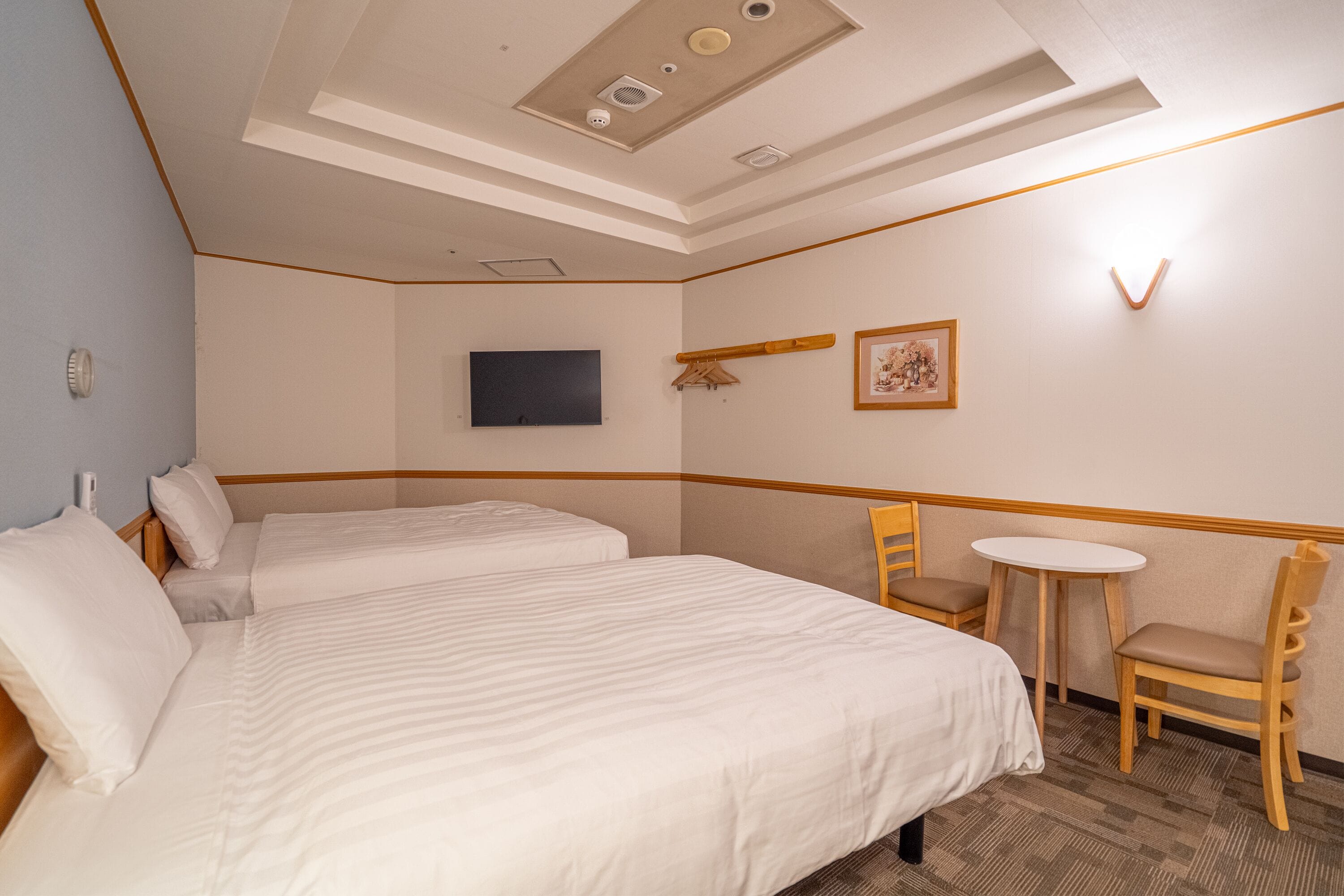 Hotellihuone, jossa on kaksi sänkyä, pieni pöytä ja tuoli.