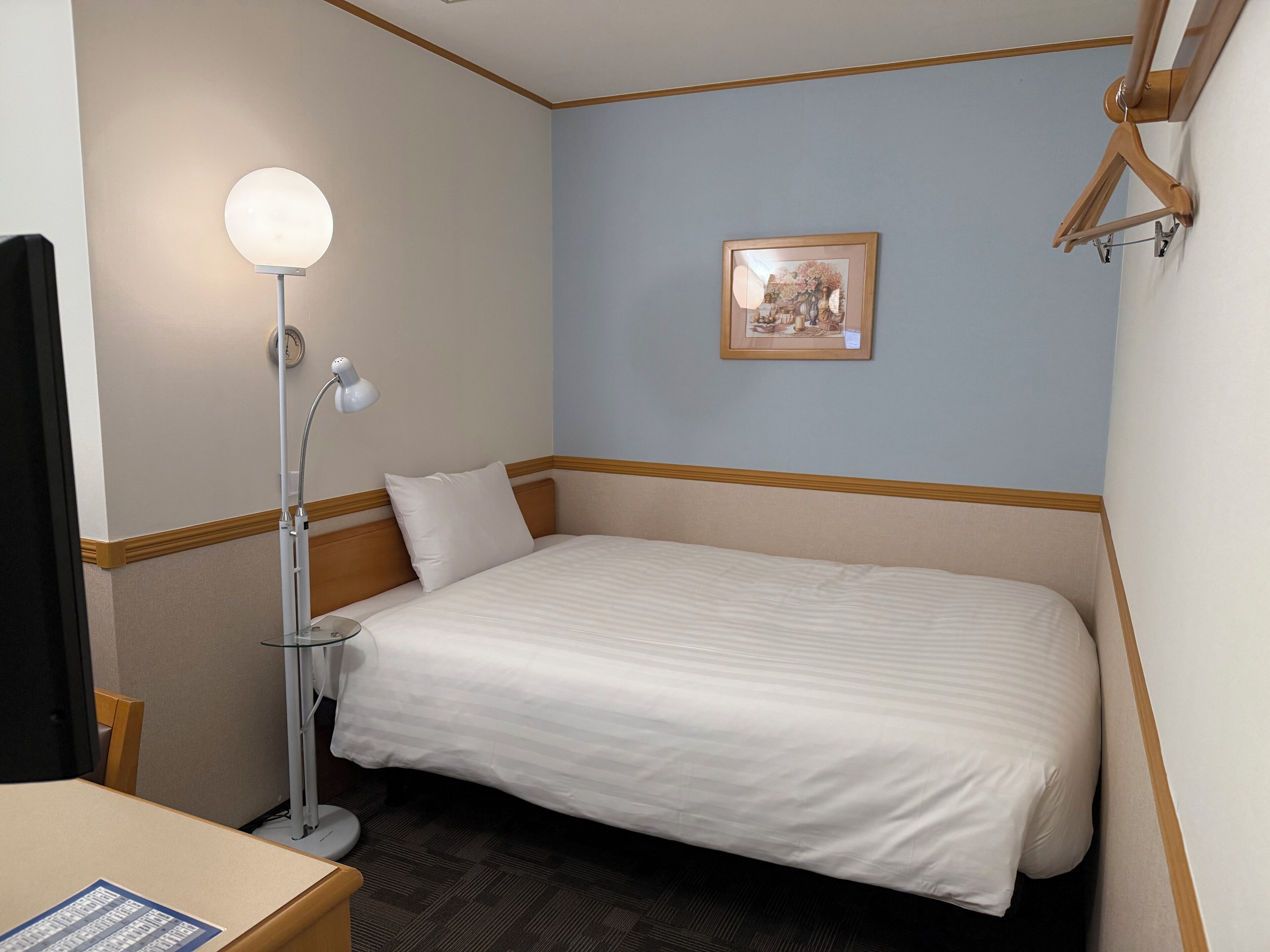 A hotel room with a single bed, a desk, a chair, a lamp, and a framed picture on the wall.
