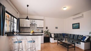 A modern kitchen with a central island, bar stools, a striped sofa, and a coffee table. - Apartamentos Alberto (Pajara)