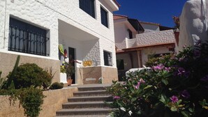 A white building with a stone facade, a balcony, and steps leading to the entrance. - Apartamentos Alberto (Pajara)