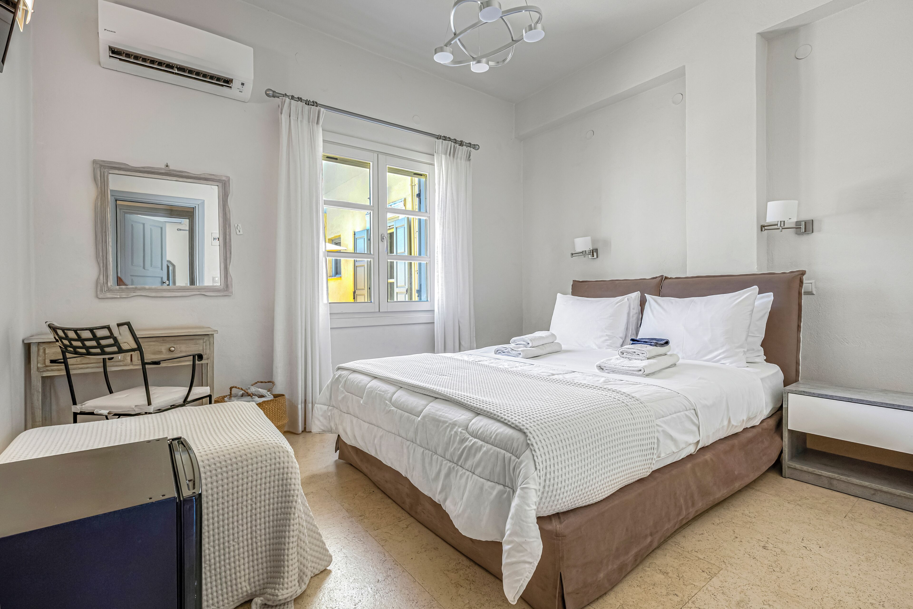 Un dormitorio con cama, escritorio, silla, ventana con cortinas y equipo de aire acondicionado.