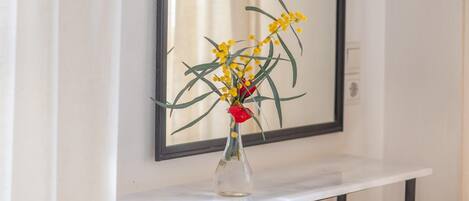 A clear view of a vase with yellow flowers and a red rose on a white shelf against a wall with a mirror.
