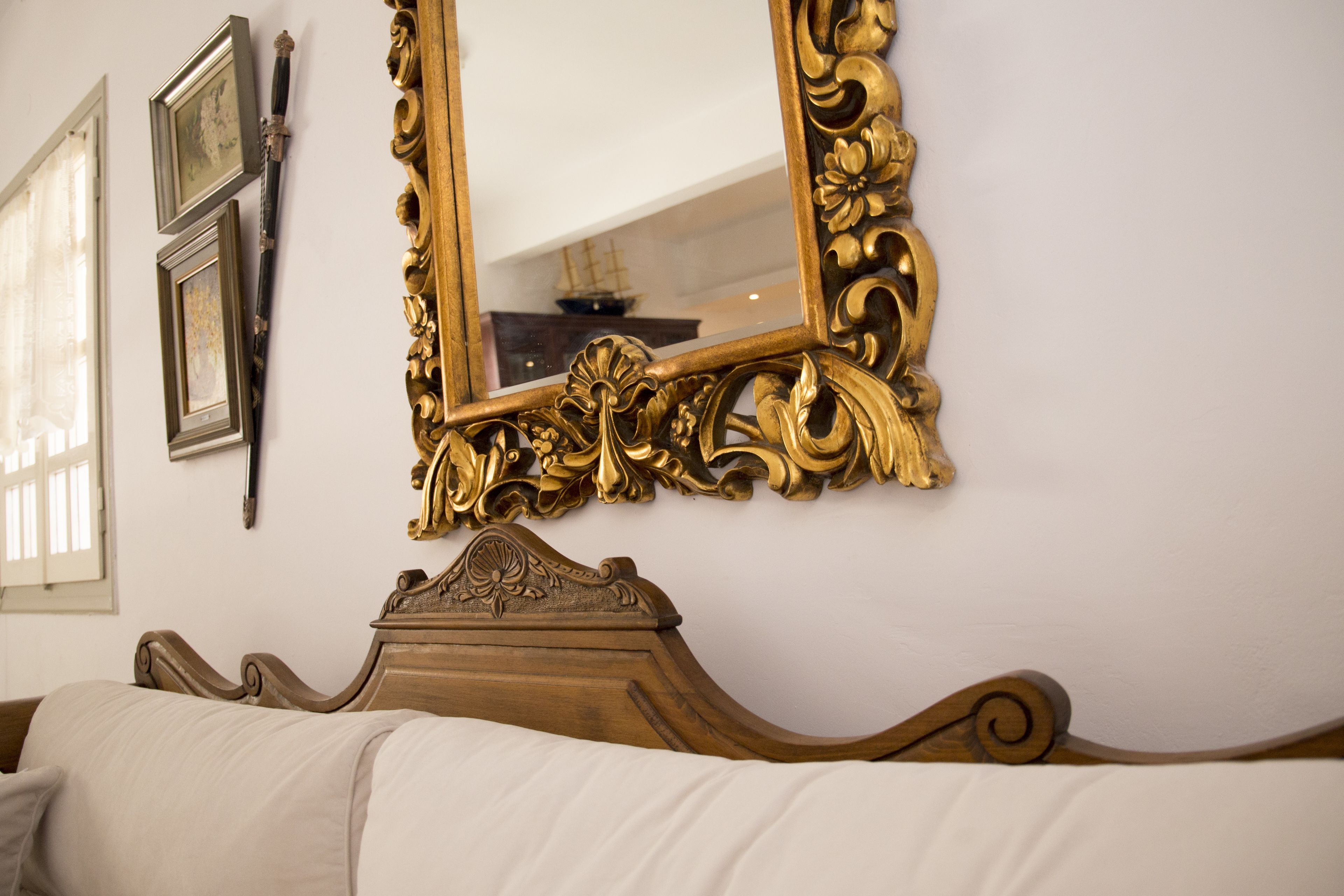 Un dormitorio con una cama de madera, un espejo grande y ornamentado, y dos cuadros en la pared.