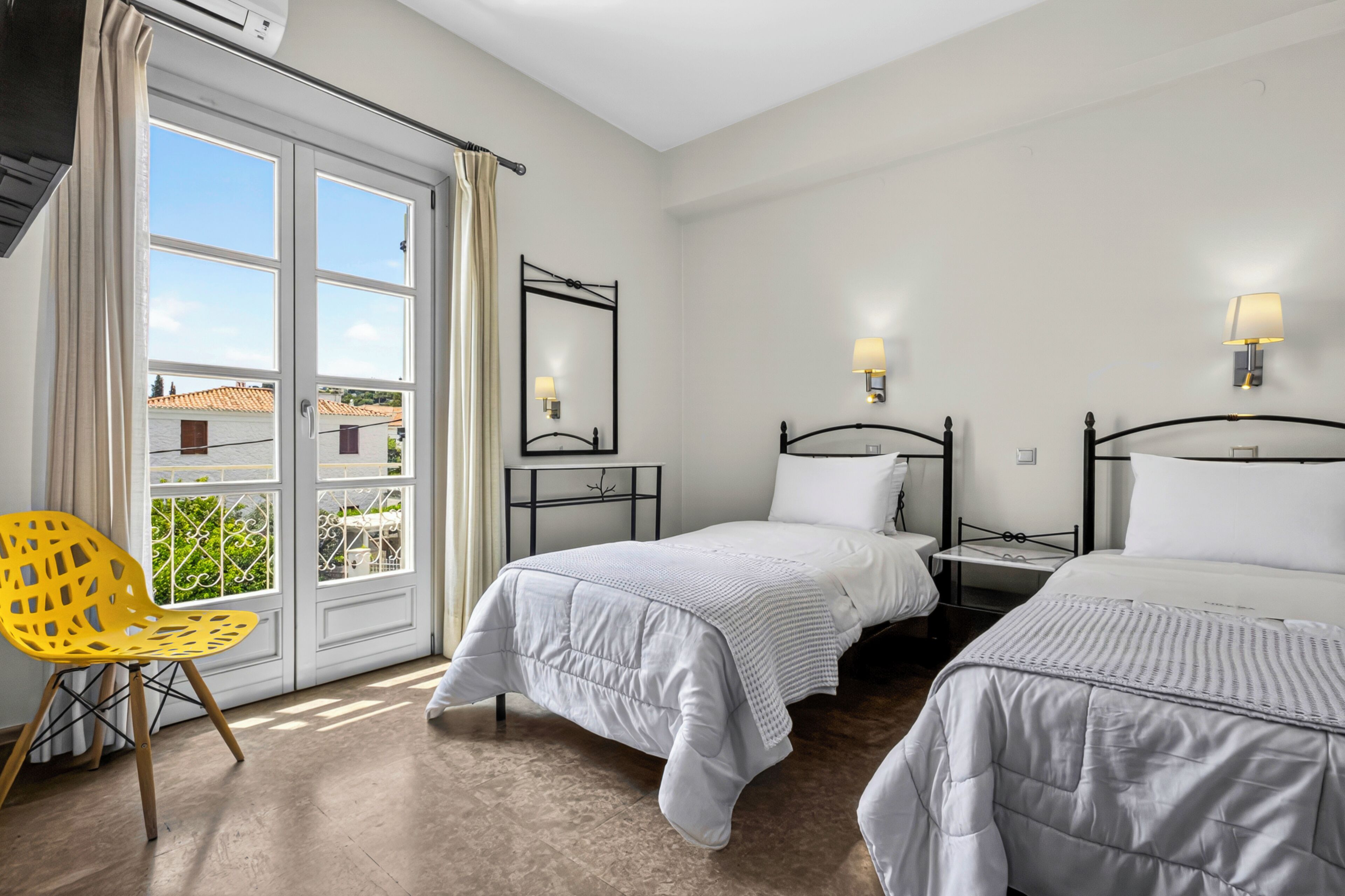 A hotel room with two beds, a chair, a window with curtains, and a view of buildings outside.