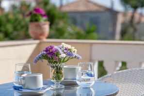 A table with a vase of flowers, two cups, and a glass of water on a balcony.