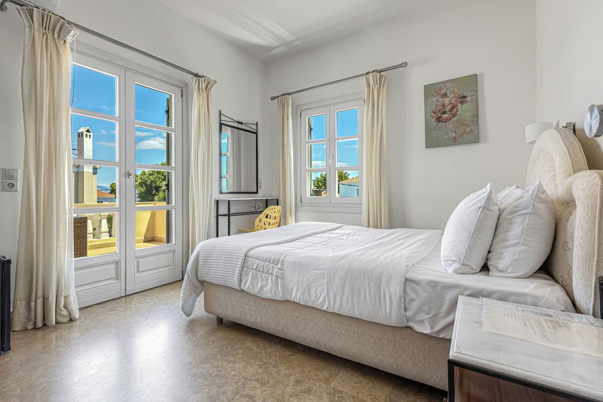 Quarto com cama, mesa de cabeceira, cadeira e janela com cortinas.