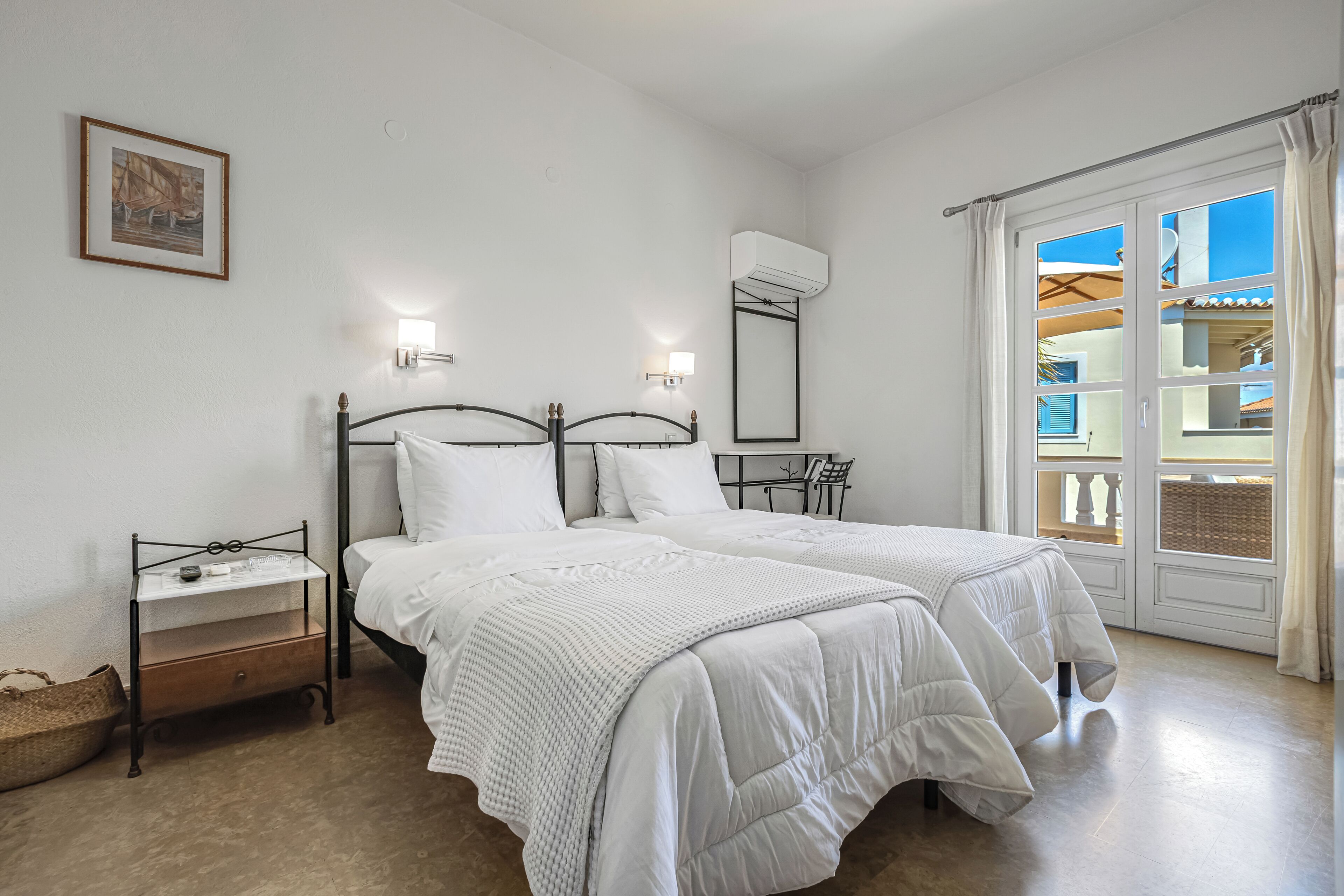 A bedroom with two beds, a bedside table, a wall-mounted air conditioner, and a window with curtains.