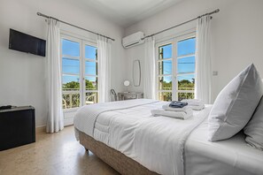 A bedroom with a bed, a TV, a desk, and a balcony view. - Mimoza (Spetses)