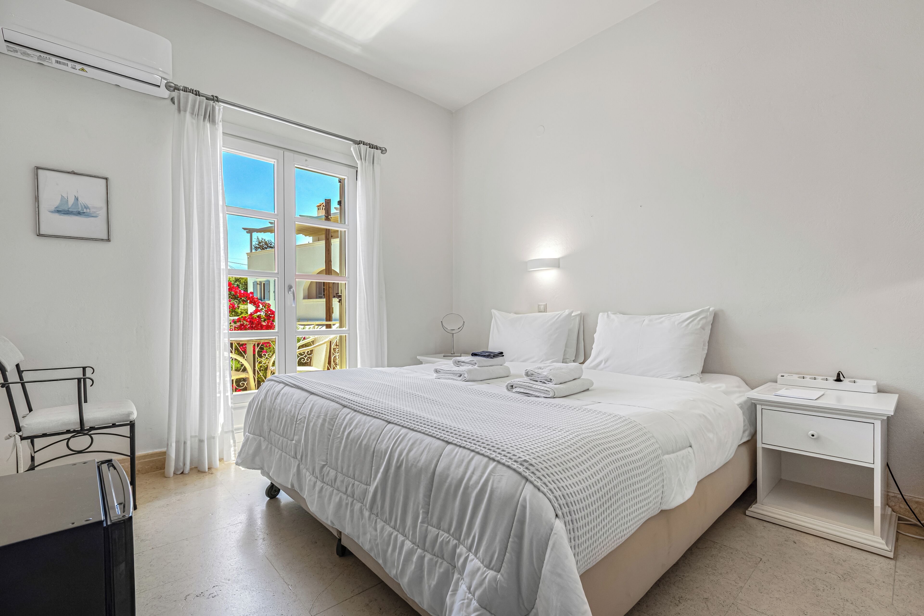 A bedroom with a bed, a bedside table, a chair, a window with curtains, and a wall-mounted light.