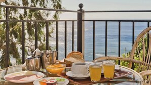 Une table en verre avec des aliments pour le petit-déjeuner, une chaise en osier et une vue sur la mer.