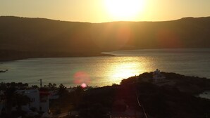 Vista del atardecer en la costa con mar tranquilo, silueta de una colina y un pequeño edificio en primer plano.