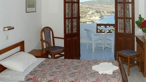 Une chambre à coucher comprenant un lit, une chaise, une petite table et un balcon avec vue sur la mer et les collines.