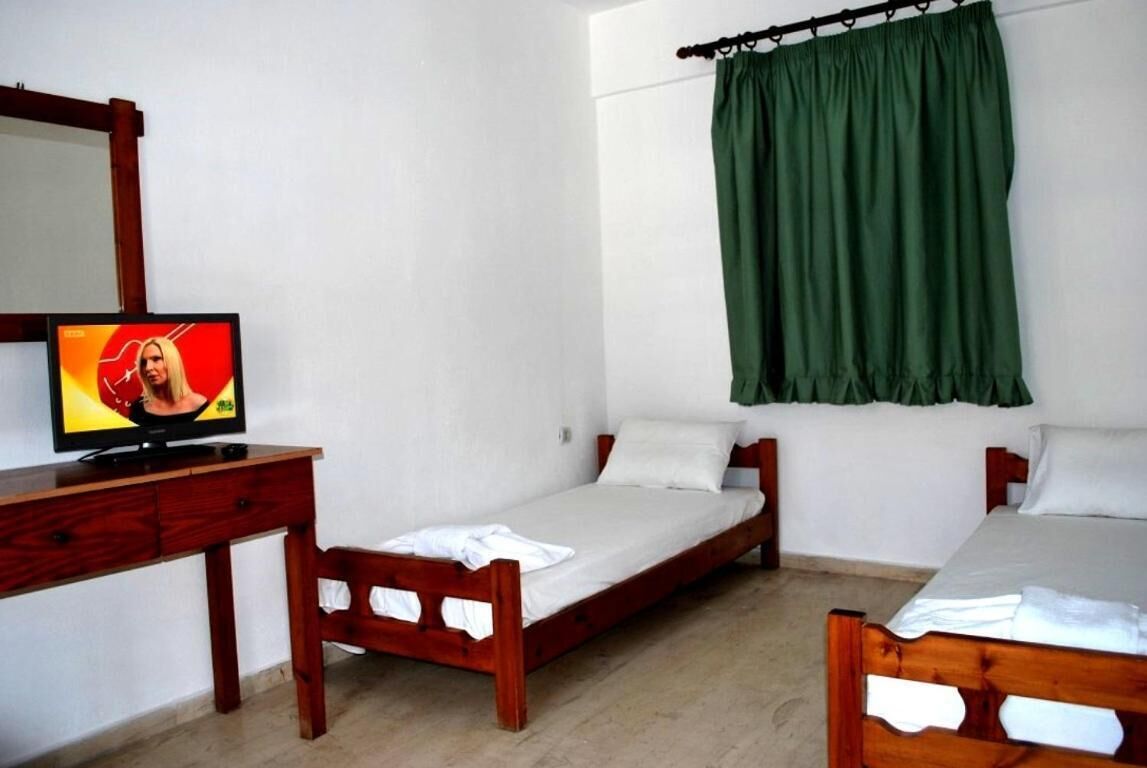 A small, clean room with a single bed, a wooden desk with a television, and a green curtain.