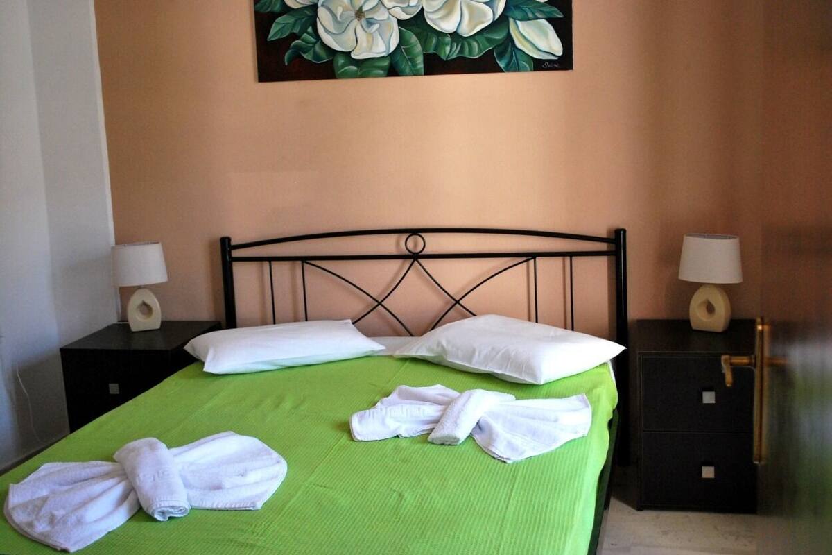 Ein ordentlich bezogenes Bett mit grüner Bettwäsche, zwei weißen Kissen und einem Set weißer Handtücher an der Kopfteil.