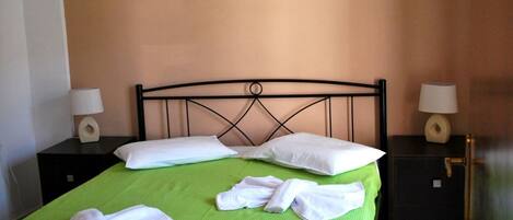 A neatly made bed with green bedding, two white pillows, and a set of white towels on a headboard.