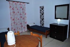 A room with a bed, a bedside table with a lamp, a wooden chair, a small table, and a decorative wall piece. - Koula Apartments (Hersonissos)