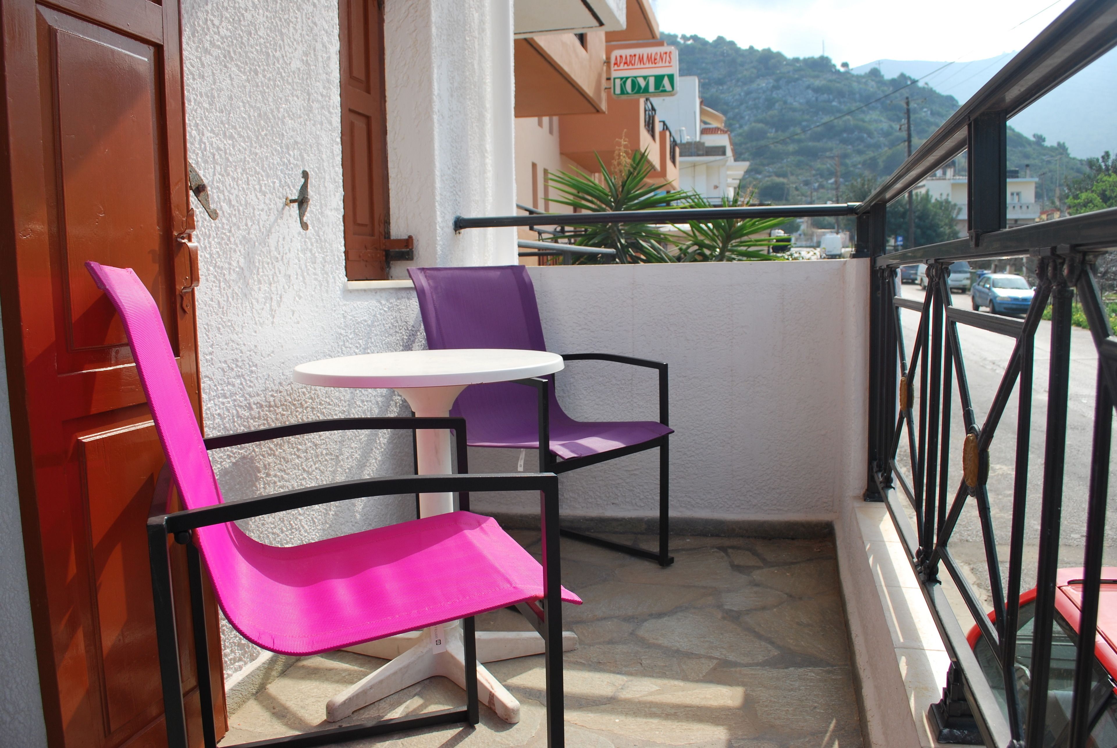 A balcony with two chairs and a small table, a wooden door, and a sign for "Apartments Toyota".