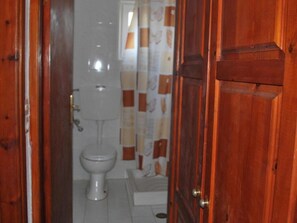 A bathroom with a toilet, a shower curtain, and a wooden door. - Koula Apartments (Hersonissos)