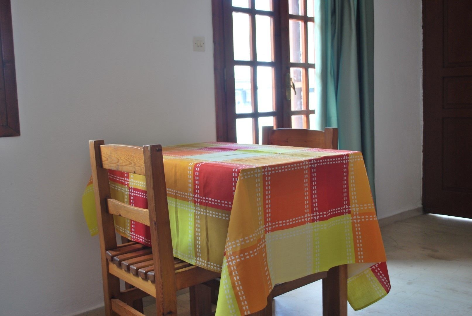 A room with a wooden chair and table, a window with curtains, and a door.