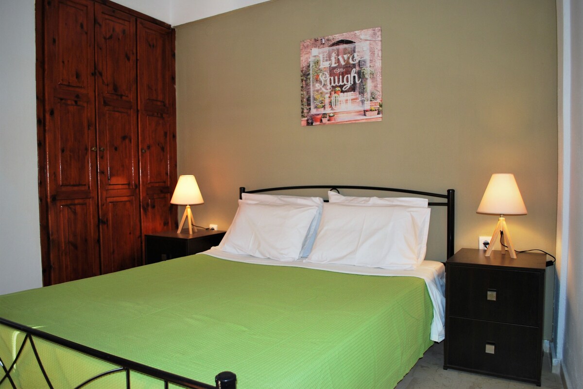 A single bed with a green bedspread, two bedside tables with lamps, and a wooden wardrobe.
