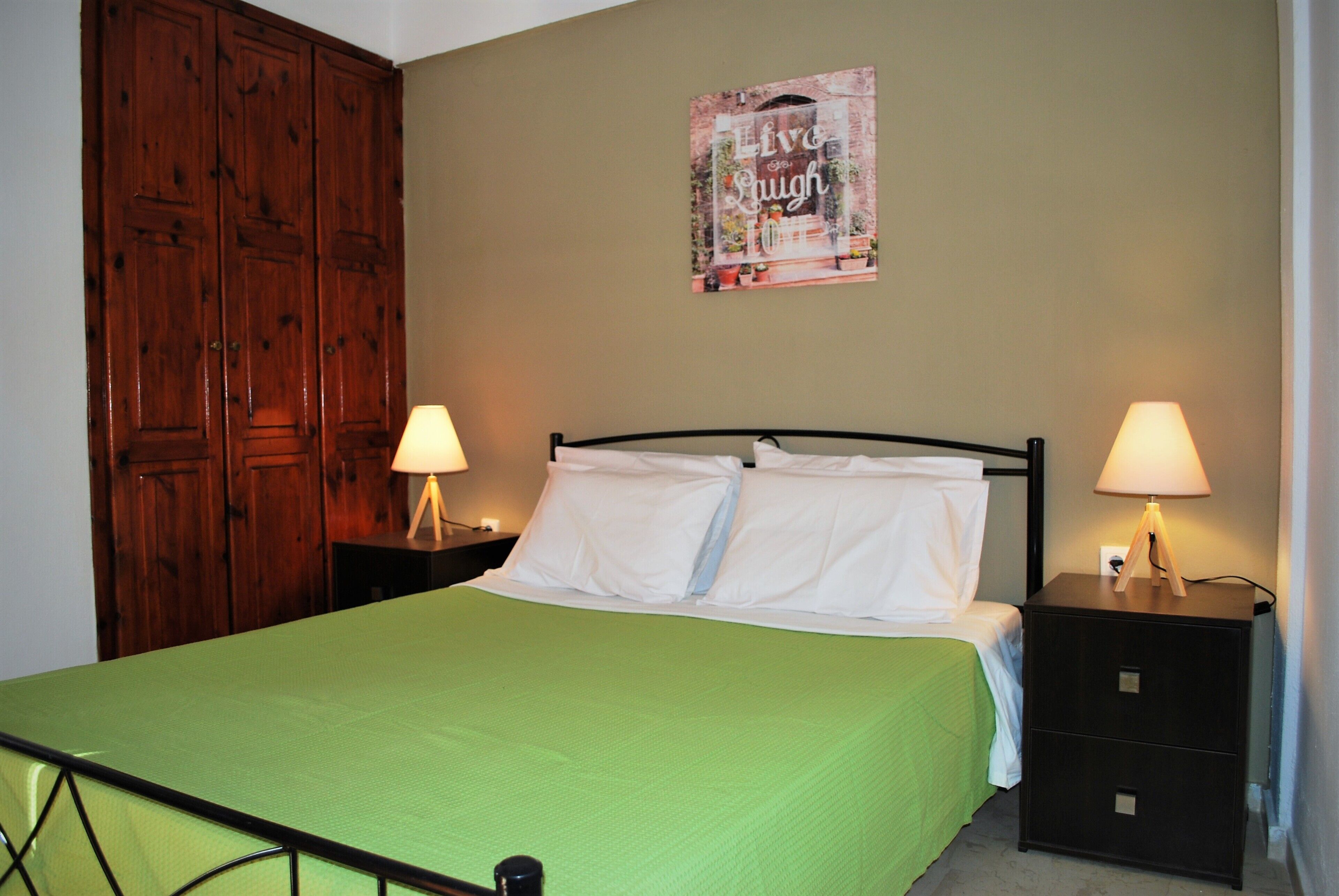 A bed with a green bedspread, two bedside tables with lamps, a wooden wardrobe, and a wall with a poster.