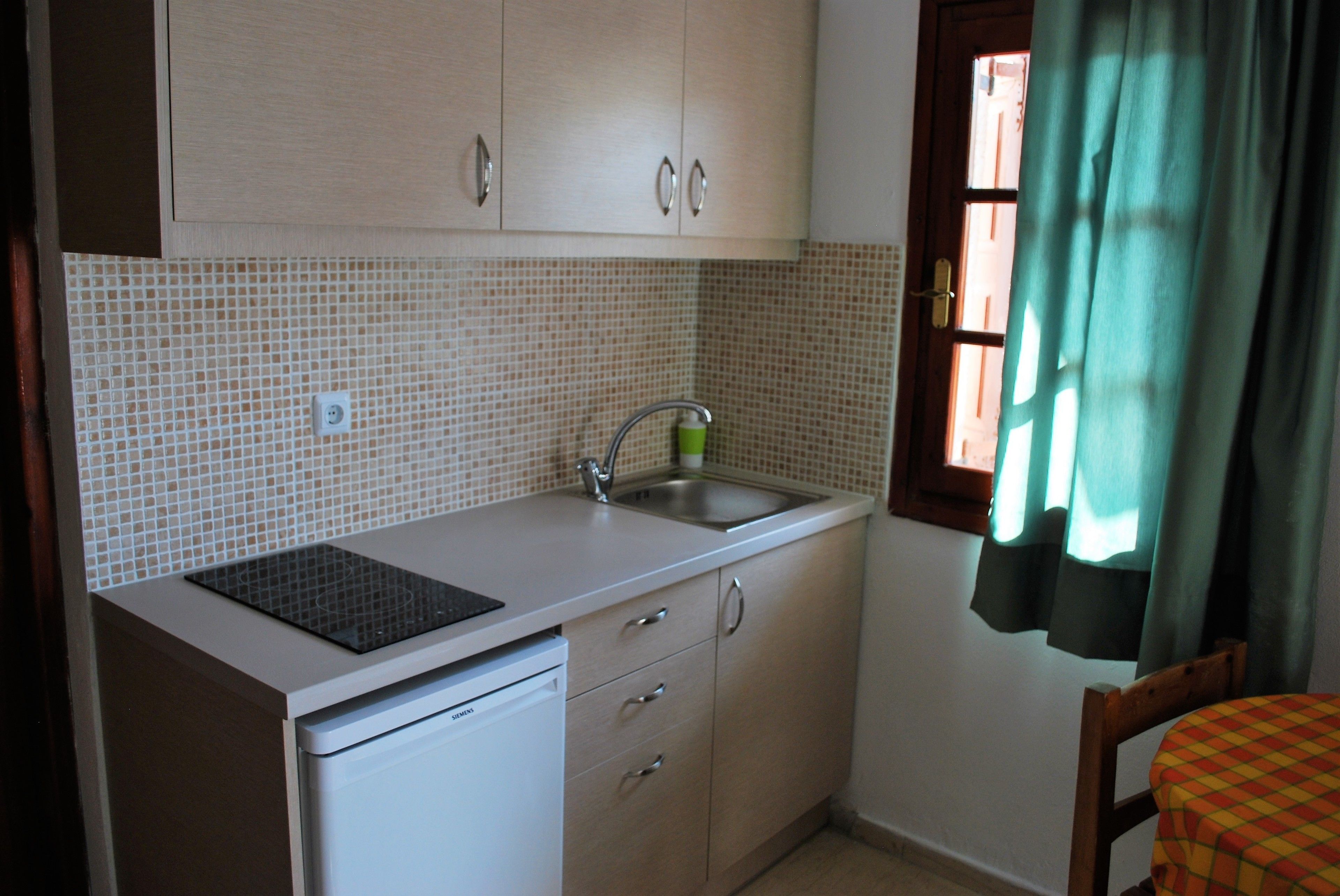 Uma cozinha compacta com pia, lava-louças e janela com cortinas.