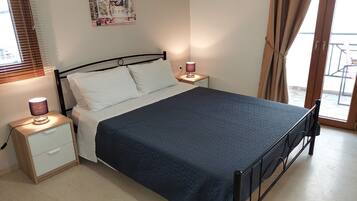 Quarto com cama, mesas de cabeceira, abajur, um pôster na parede e vista pela janela.
